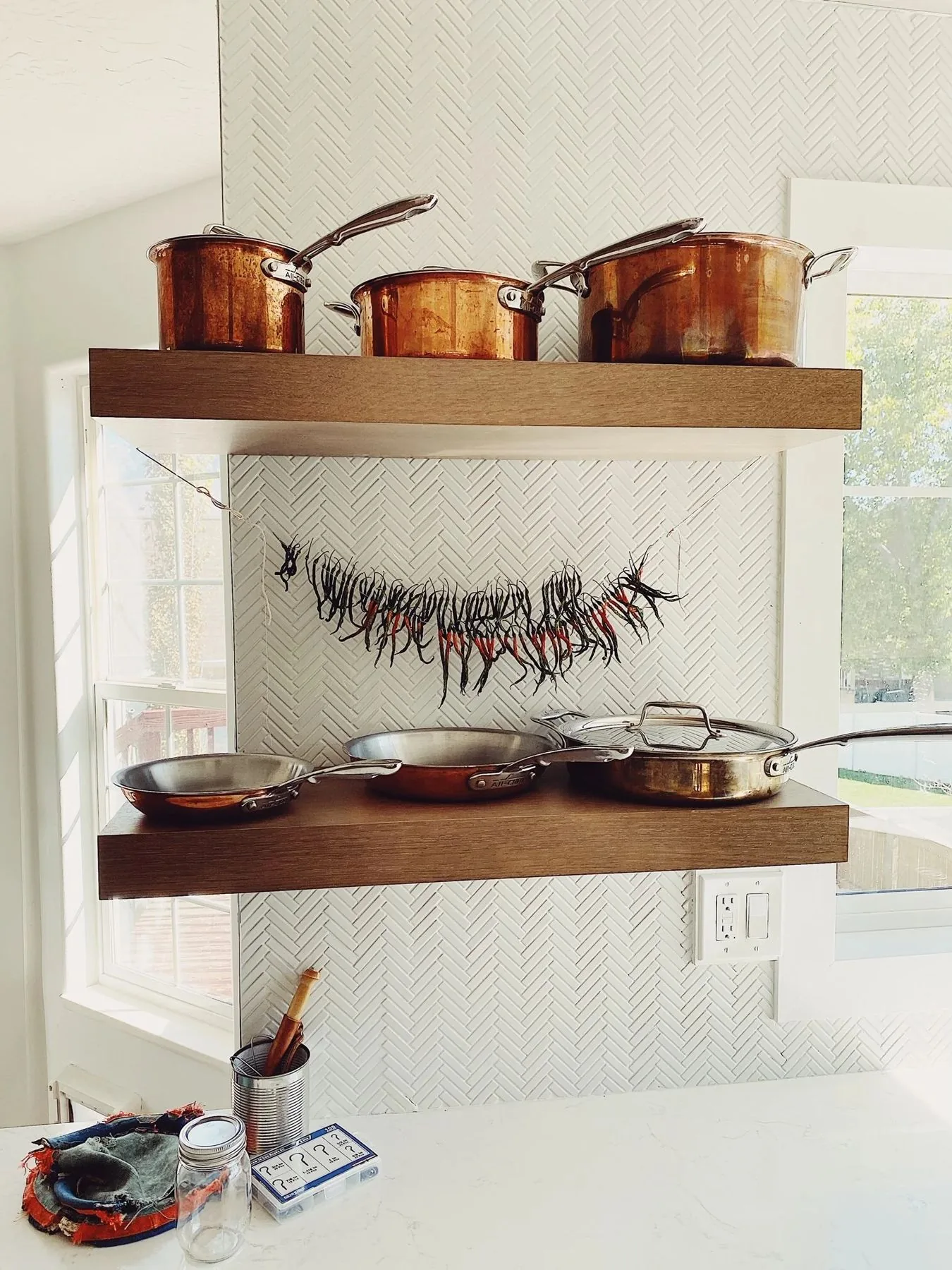Walnut floating shelves with copper cookware over herringbone tile