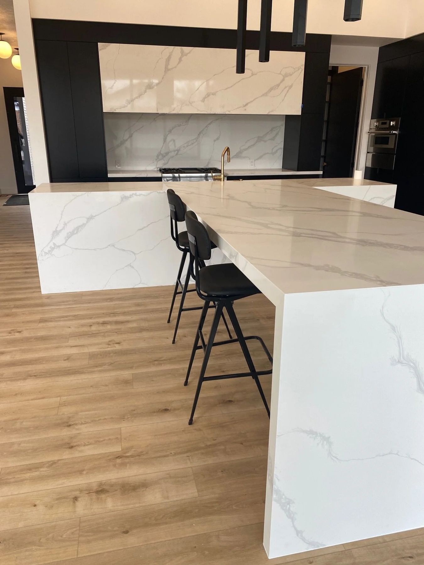 White marble waterfall island with black stools and oak flooring
