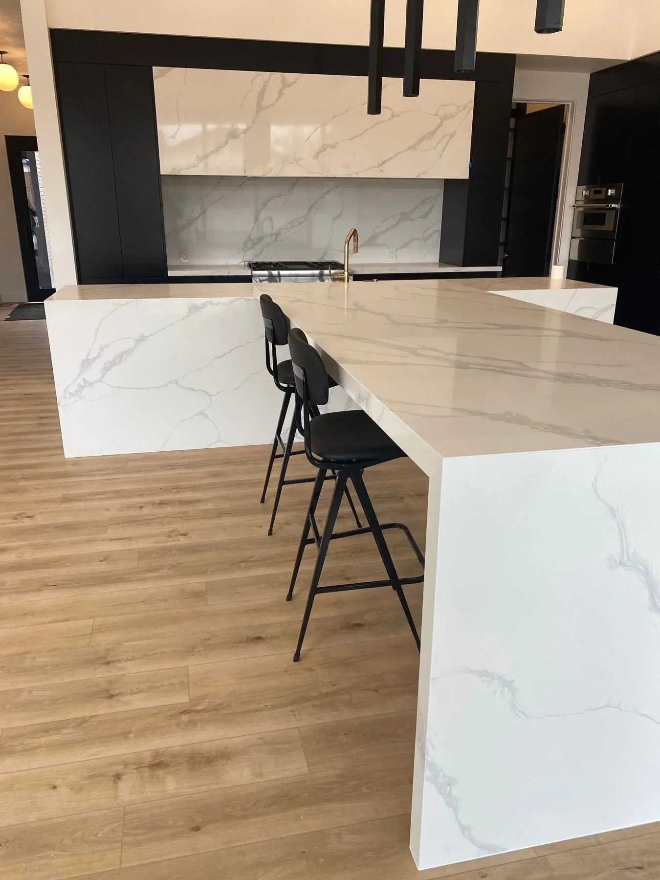 White marble waterfall island with black stools and oak flooring